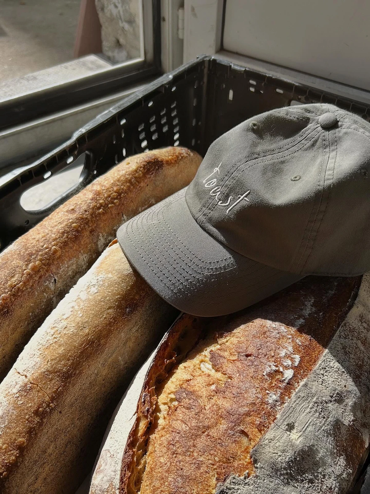 Baguettes au levain dans une caisse, casquette brodée Toast posée dessus